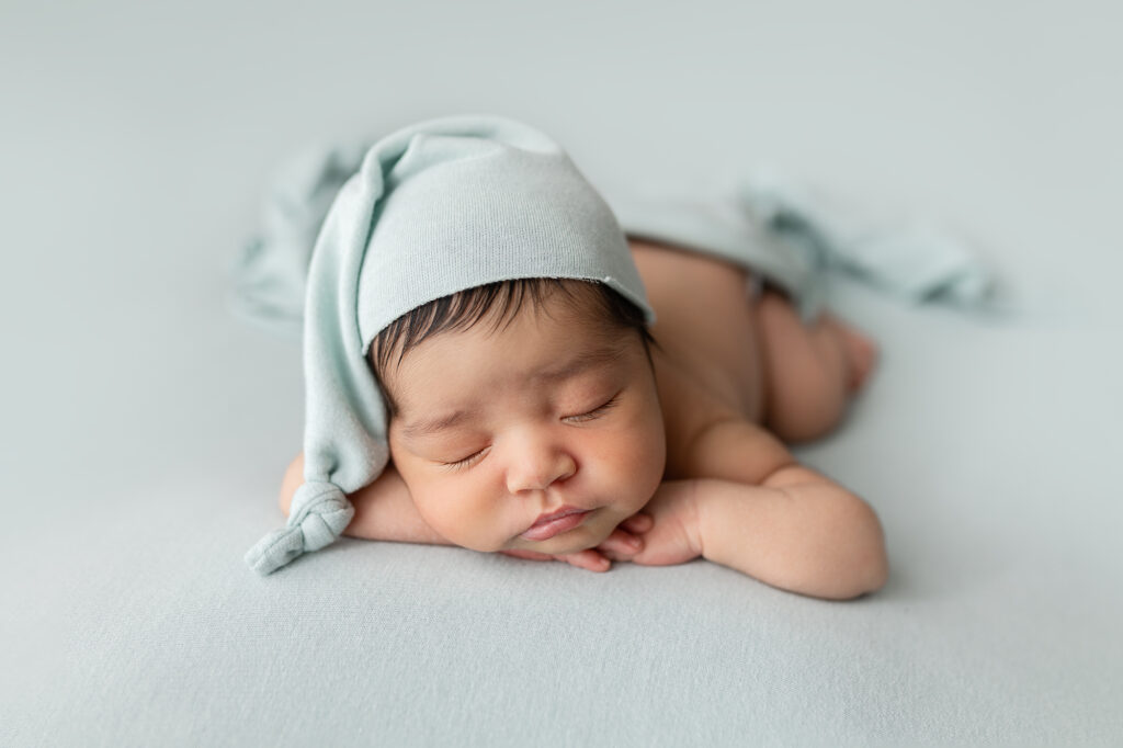 Baby boy with light blue sleepy cap posed during his newborn photography session.