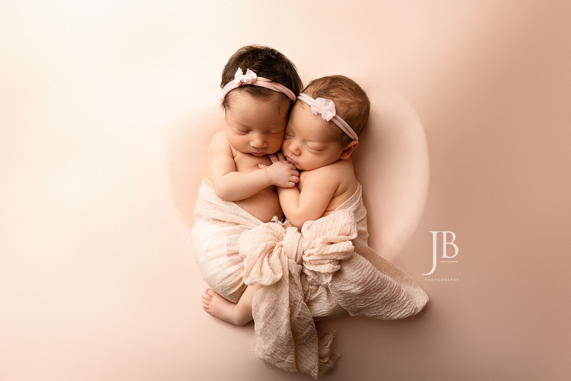 Twin newborn girls posed in a heart.