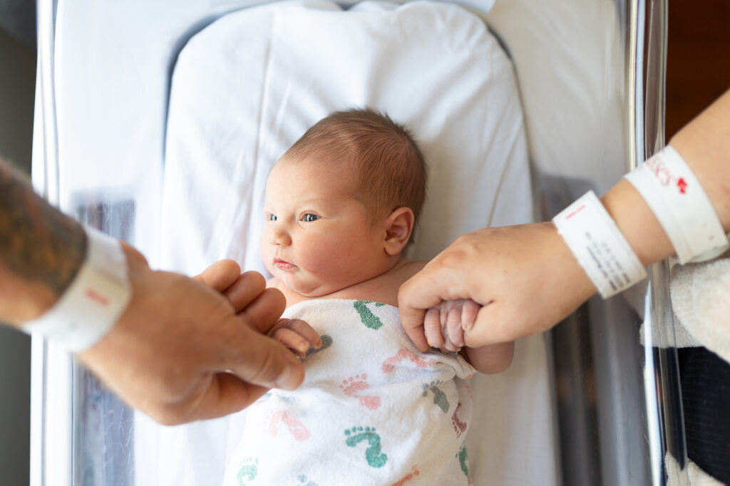 Newborn baby holding mom and dad's hands in the hospital for her Fresh 48 Newborn Session.