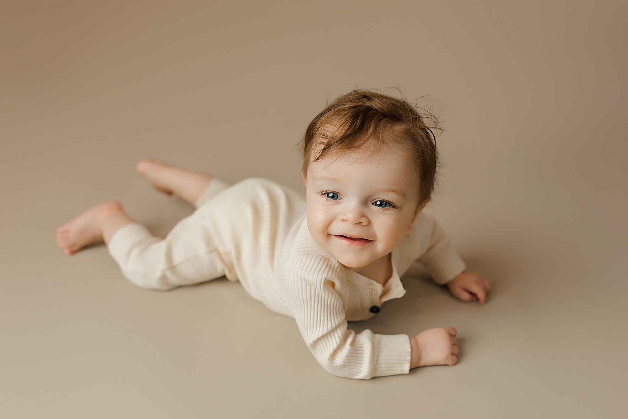 Smiling baby boy wearing a neutral colored cream onesie during his baby session at Jennifer Brandes Photography.