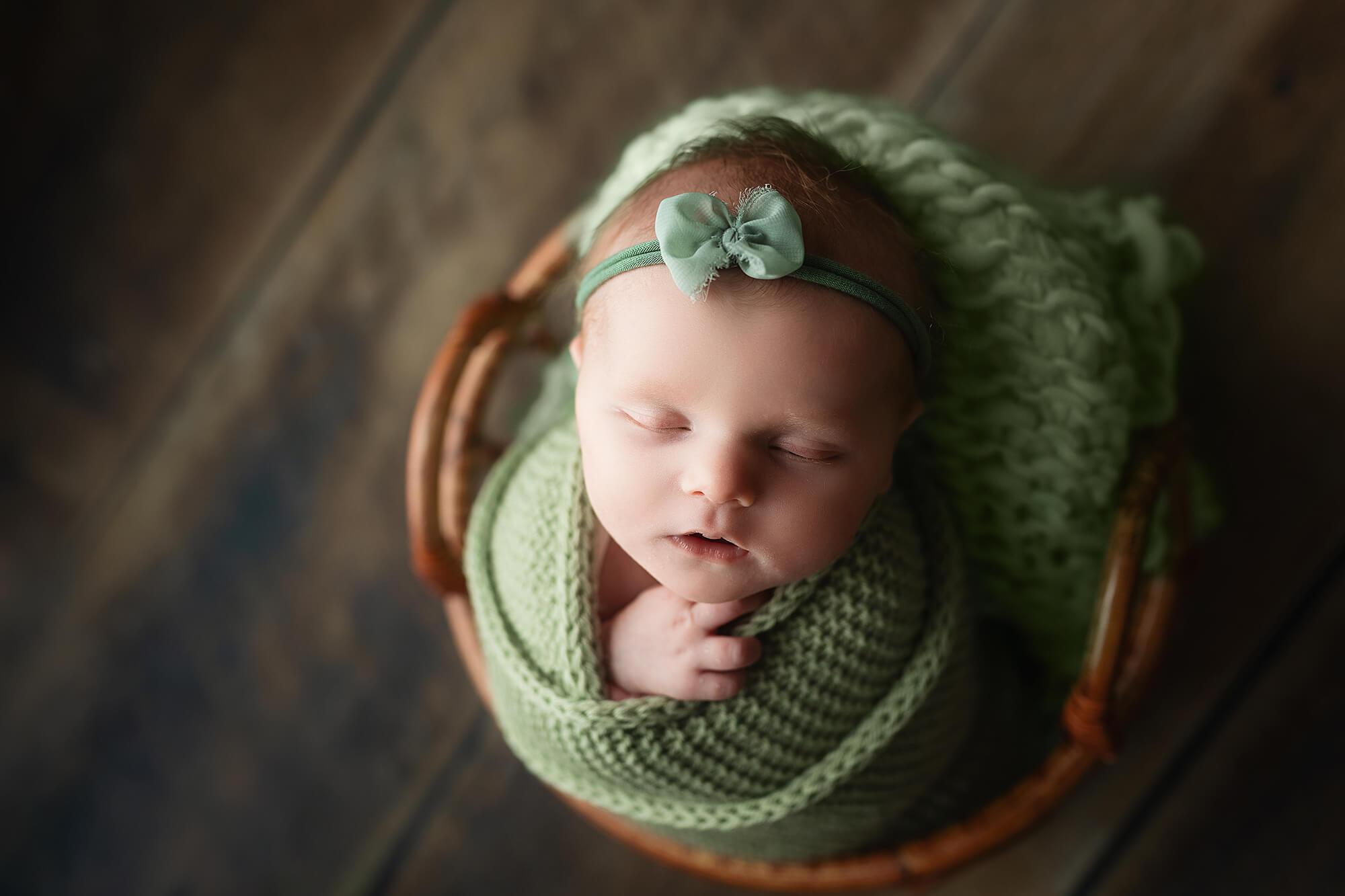 Baby girl wearing a green headband and wrapped in a green knitted blanket during her newborn session.