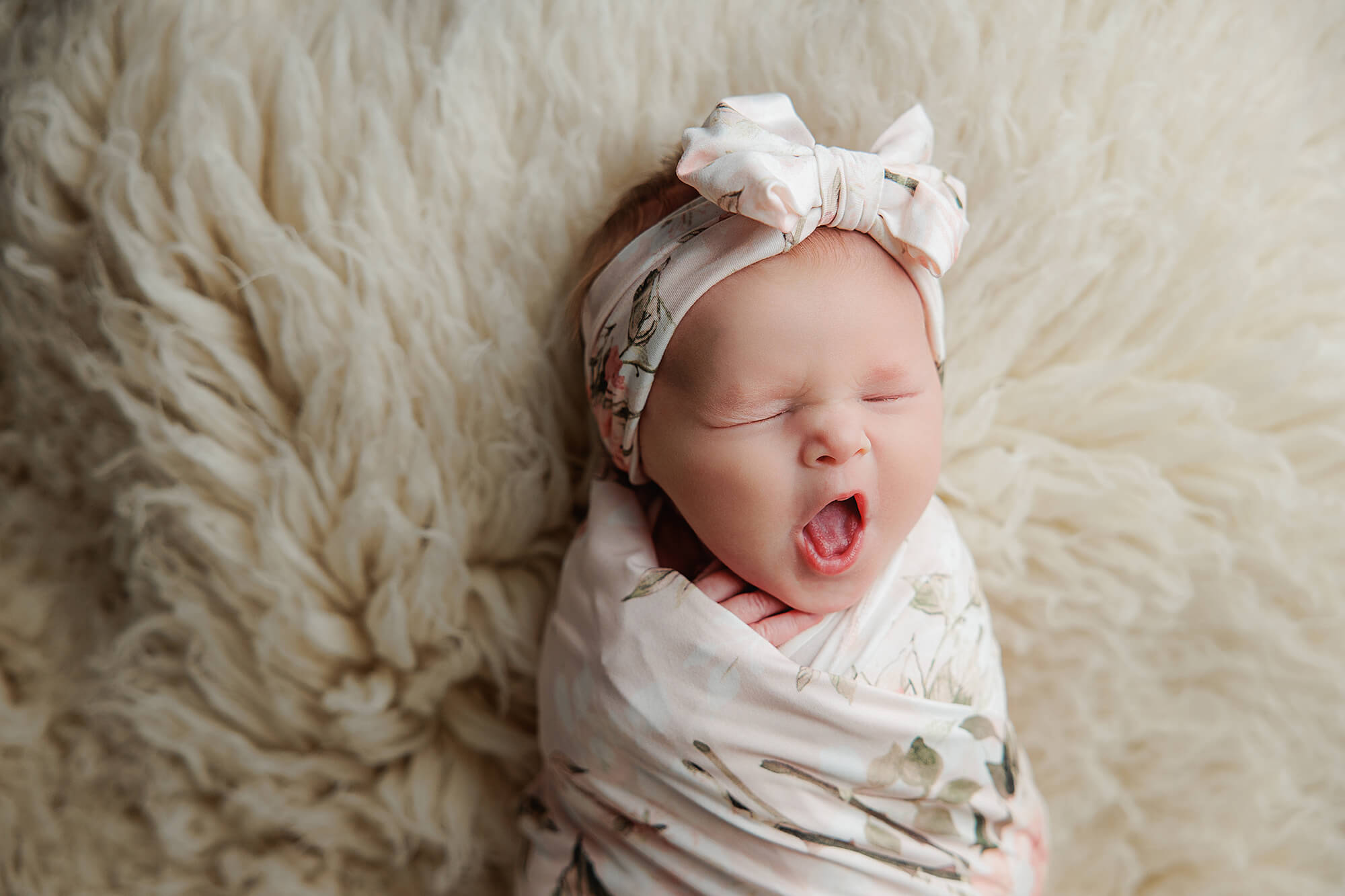 Newborn girl yawning and wrapped in floral for her newborn photography session that was booked early.