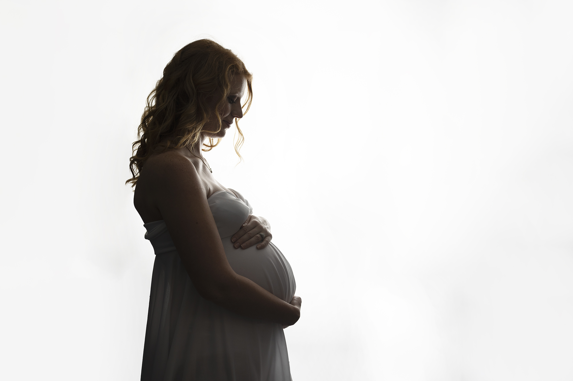 Silhouette of expectant mother wearing a white dress.