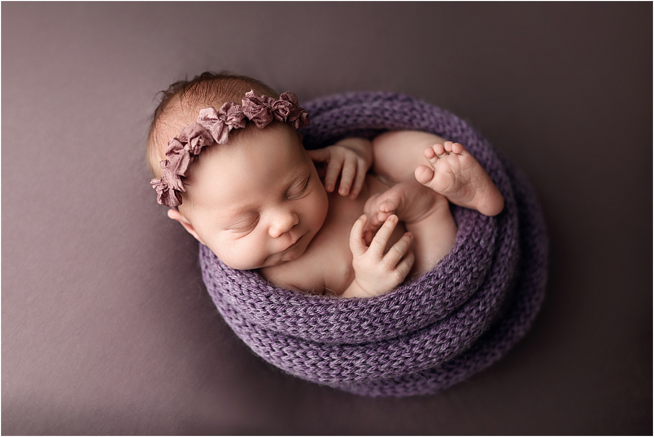 Newborn baby girl wrapped in purple and posed by her newborn photographer, Jennifer Brandes of Minnesota.