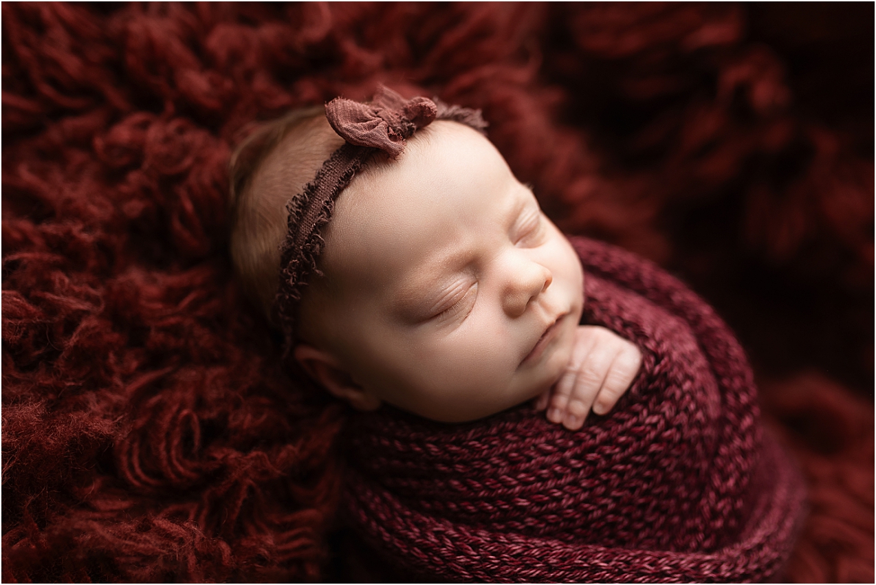 Baby girl wrapped in garnet during her newborn photography session.