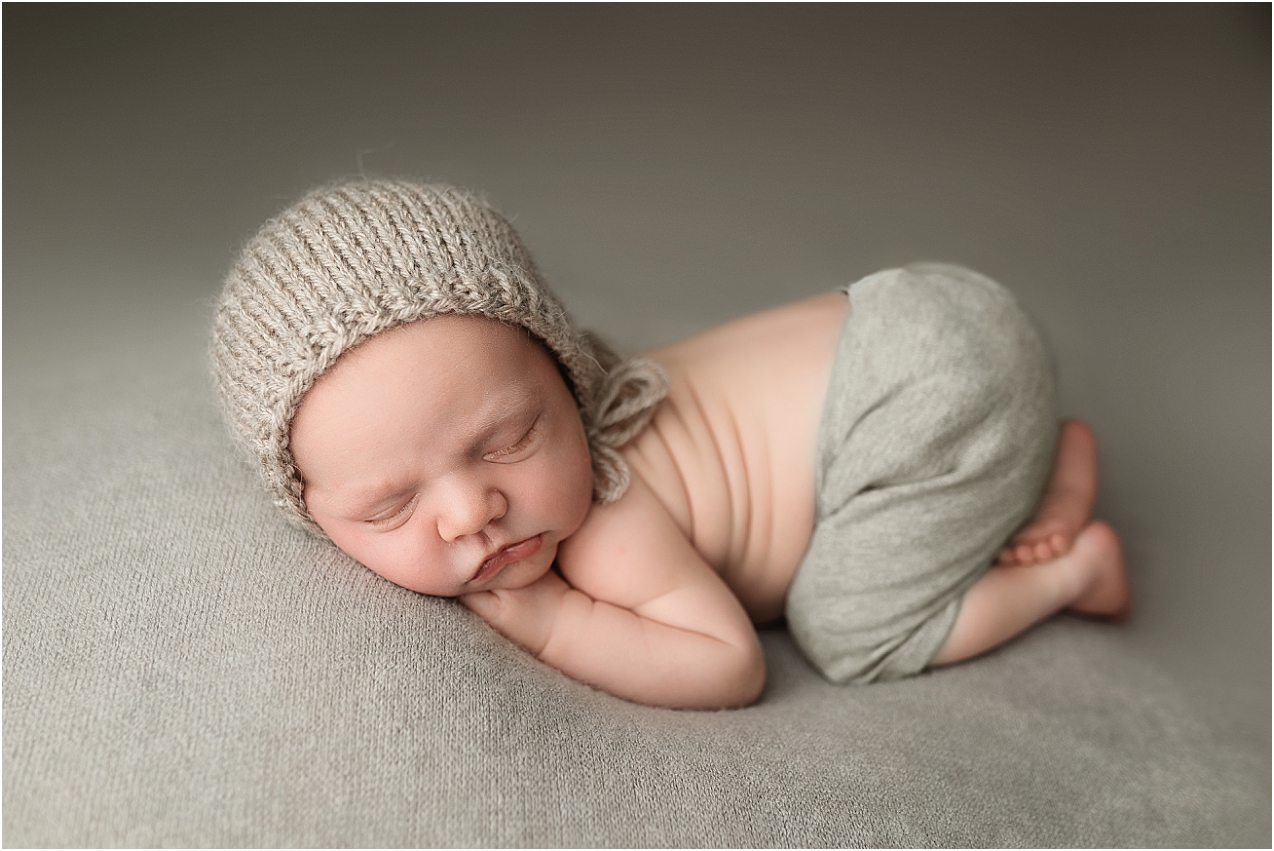 Baby boy wearing a grey bonnet and matching pants, provided by the newborn photographer in Southern Minnesota.