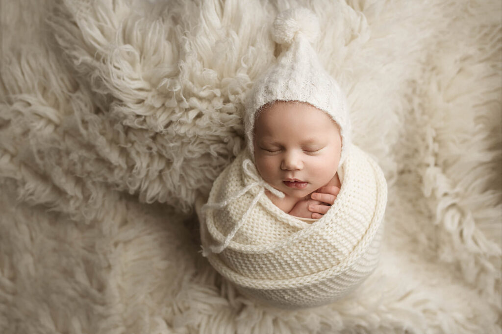 Baby boy wrapped in a white hand knitted wrap with sleepy cap.