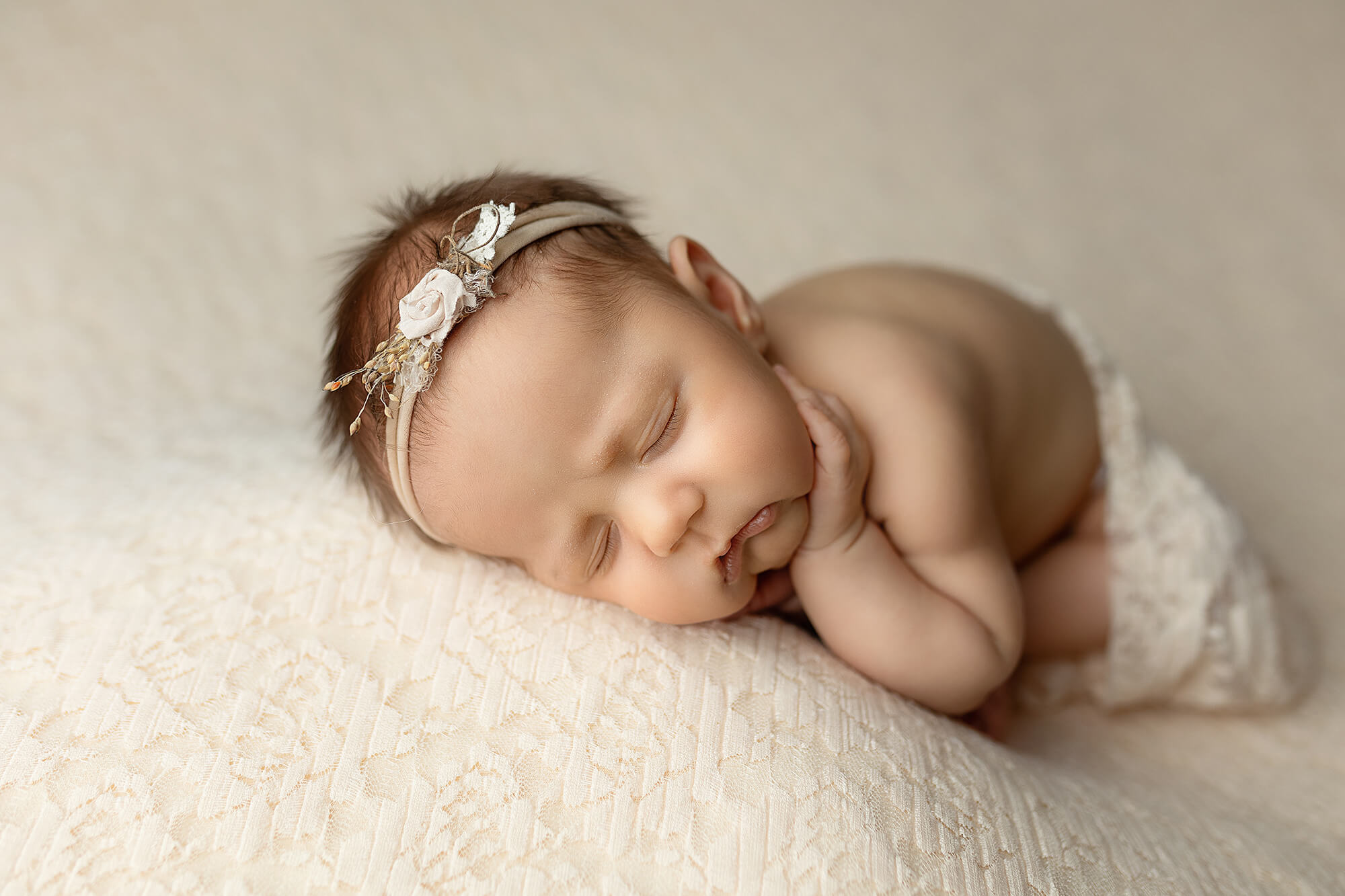 Newborn girl sleeping on a neutral colored backdrop.